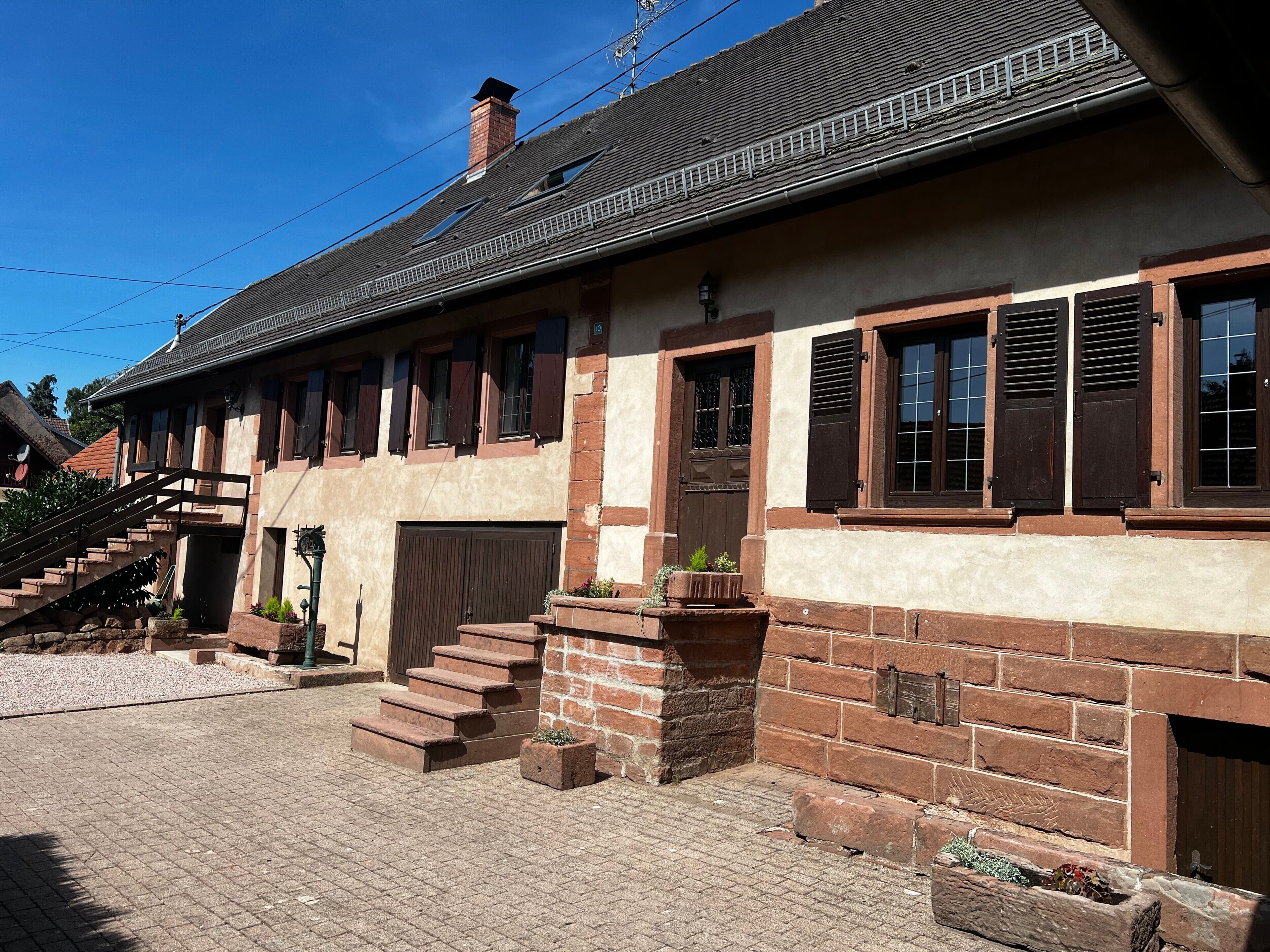 Ein traditionelles Gebäude mit Ziegelverkleidung, einer Treppe, die zu einer Tür führt, und einem strahlend blauen Himmel.