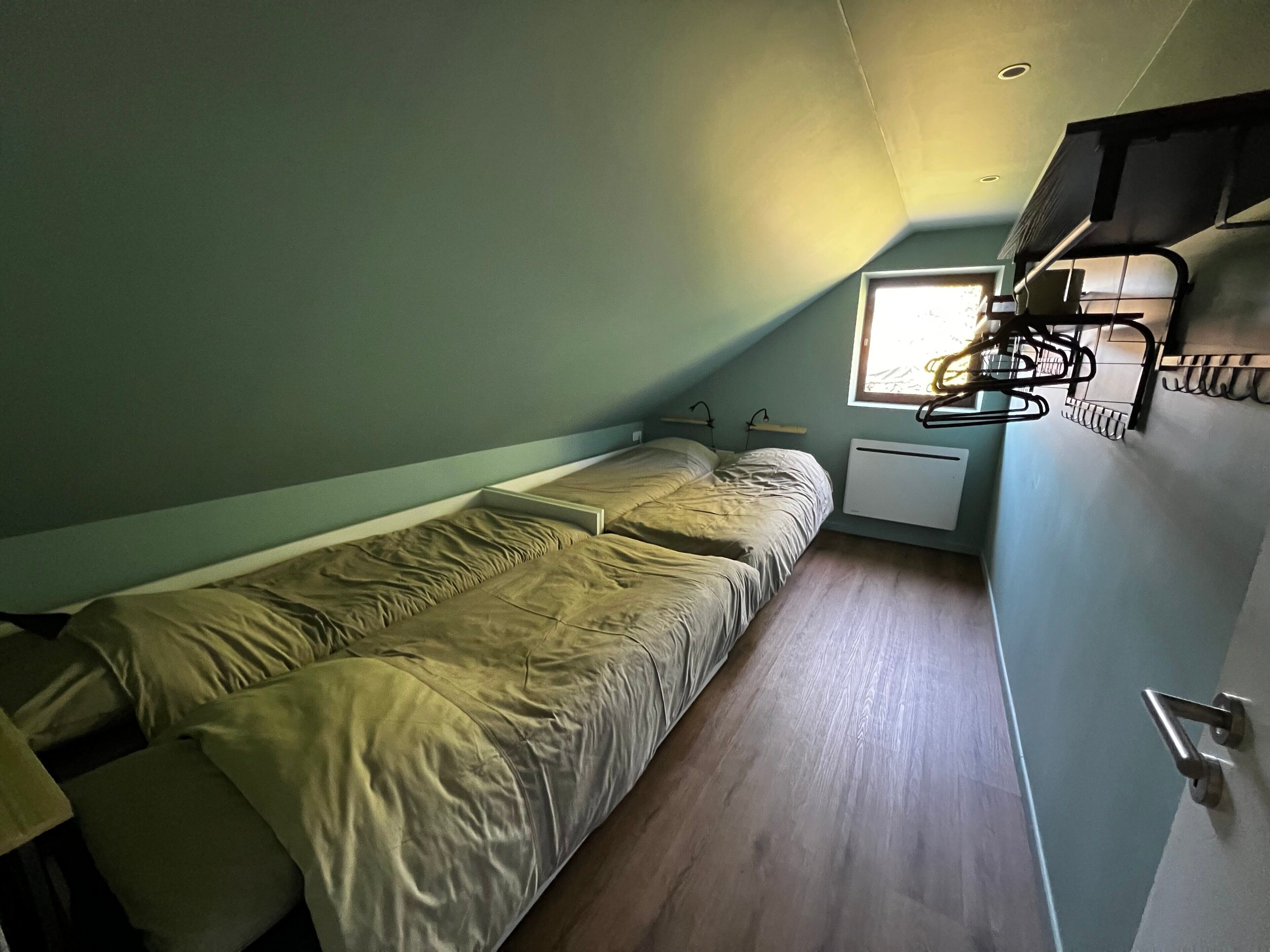 A small, single-bed room with a sloped ceiling, a window, a radiator, and a wall-mounted rack.