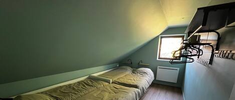 A small, single-bed room with a sloped ceiling, a window, a radiator, and a wall-mounted rack.