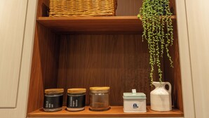 Een houten plank met potten met de tekst 'SALE', 'ZUCCHERO' en 'suiker', een witte kan en een hangende plant.