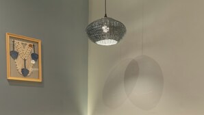 Een zithoek met eettafel, vier stoelen, een wandkleed van macramé en een hanglamp.