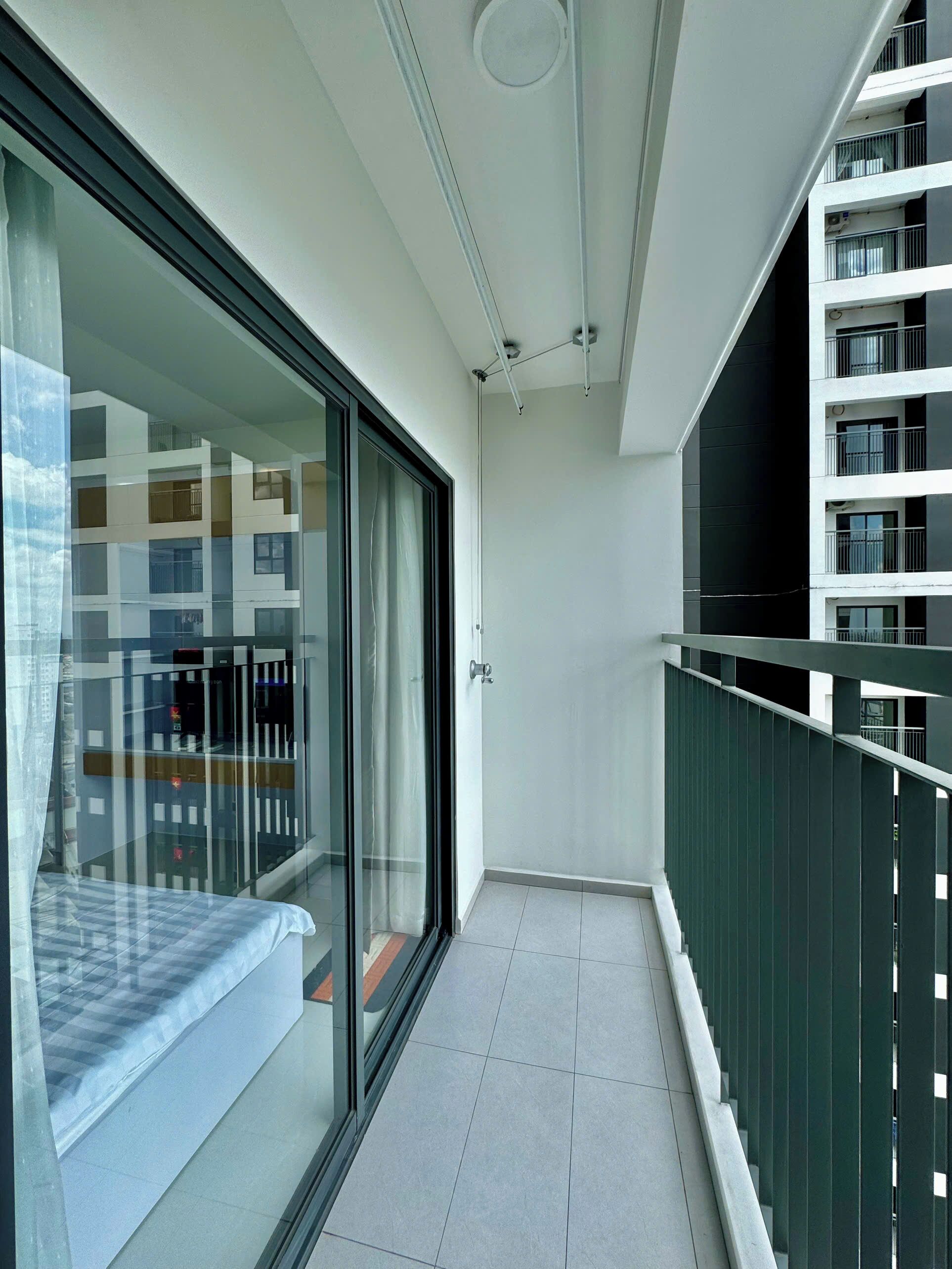 A narrow balcony with a glass door leading to a room with a bed.