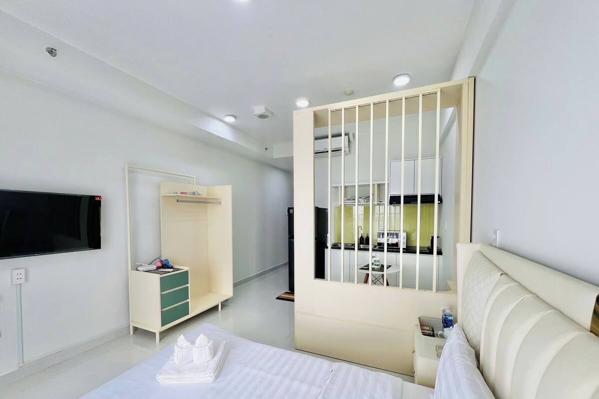 A hotel room with a bed, a TV, a wardrobe, a small table, and a kitchenette area.
