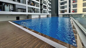A modern indoor swimming pool with a wooden deck, surrounded by multi-story residential buildings with balconies. - New Lavida (Ho Chi Minh City)