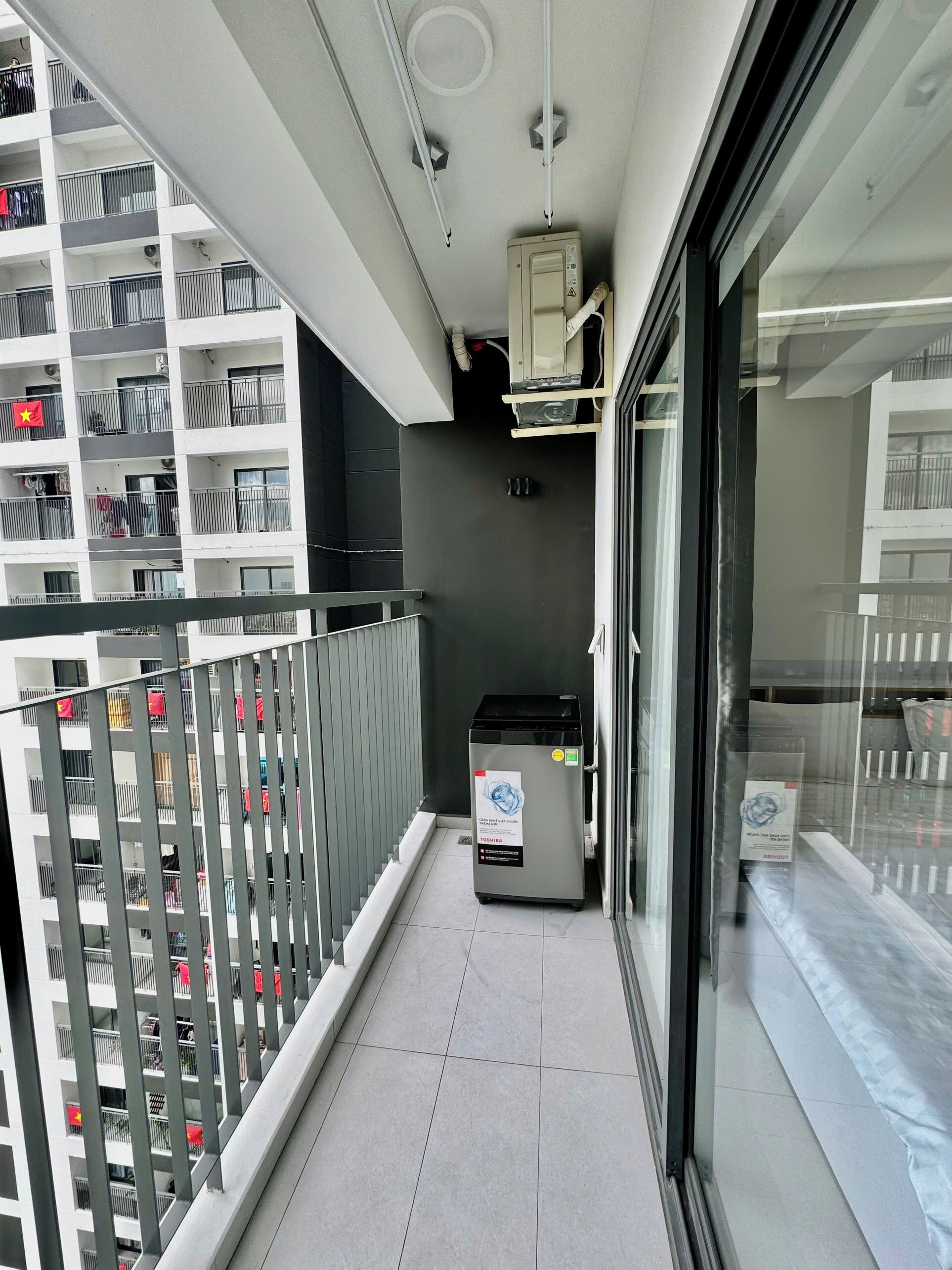 A narrow balcony with a trash bin, a glass door, and a metal railing.