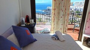 A hotel room with a bed, pillows, a small table with a kettle, and a view of the ocean and buildings. - Room + bathroom, splendid sea view, well equipped (Callao Salvaje)