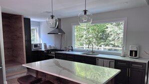 Une cuisine moderne dotée d’un grand îlot central, de meubles de rangement aux couleurs sombres et d’une fenêtre offrant une vue sur la verdure.