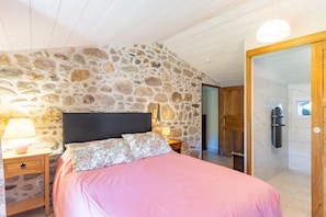 A bedroom with a stone wall, a bed with floral pillows, wooden nightstands, and a wooden door.