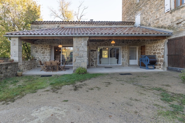 A stone building with a tiled roof, outdoor seating, and a barbecue area.