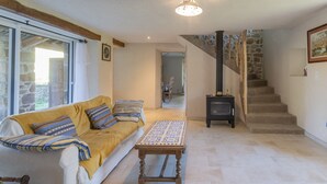 A living room with a sofa, a patterned table, a staircase, and a stone wall. - Cottage 'L'Ancienne Estable' with Private Terrace, Private Garden and Air Conditioning (Les Assions)