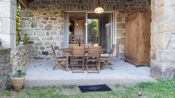 A stone building with a wooden table and chairs outside, a wooden cabinet, and a potted plant. - Cottage 'L'Ancienne Estable' with Private Terrace, Private Garden and Air Conditioning (Les Assions)