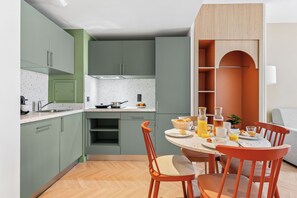 A modern kitchen with green cabinets, a dining area with a round table, and a red chair. - All Suites Appart Hôtel | Val d’Europe près de Disneyland® Paris (Serris)