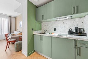 A modern kitchen with green cabinets, a white countertop, and a coffee maker. - All Suites Appart Hôtel | Val d’Europe près de Disneyland® Paris (Serris)