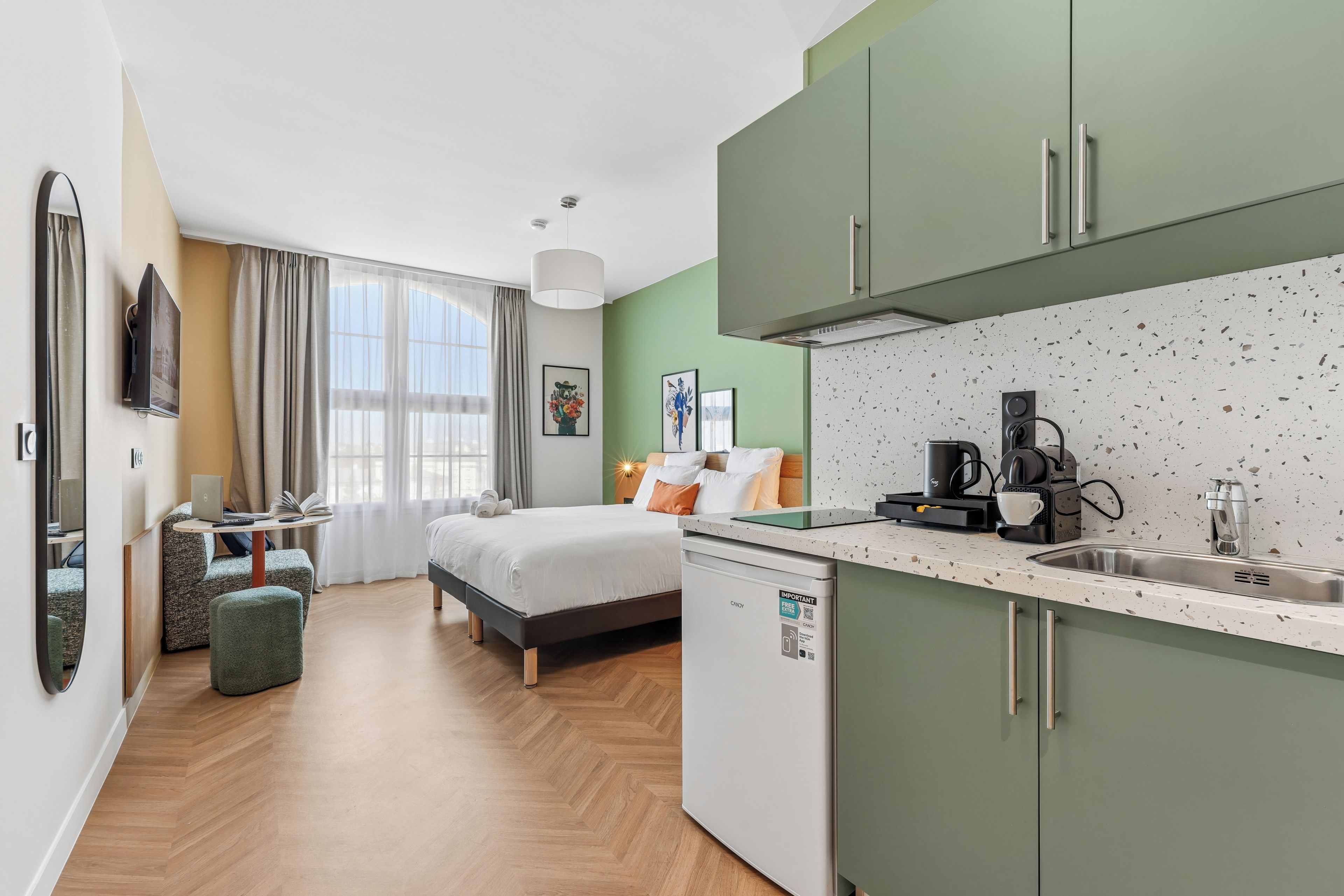 Een moderne hotelkamer met een bed, bureau, kitchenette en badkamer.