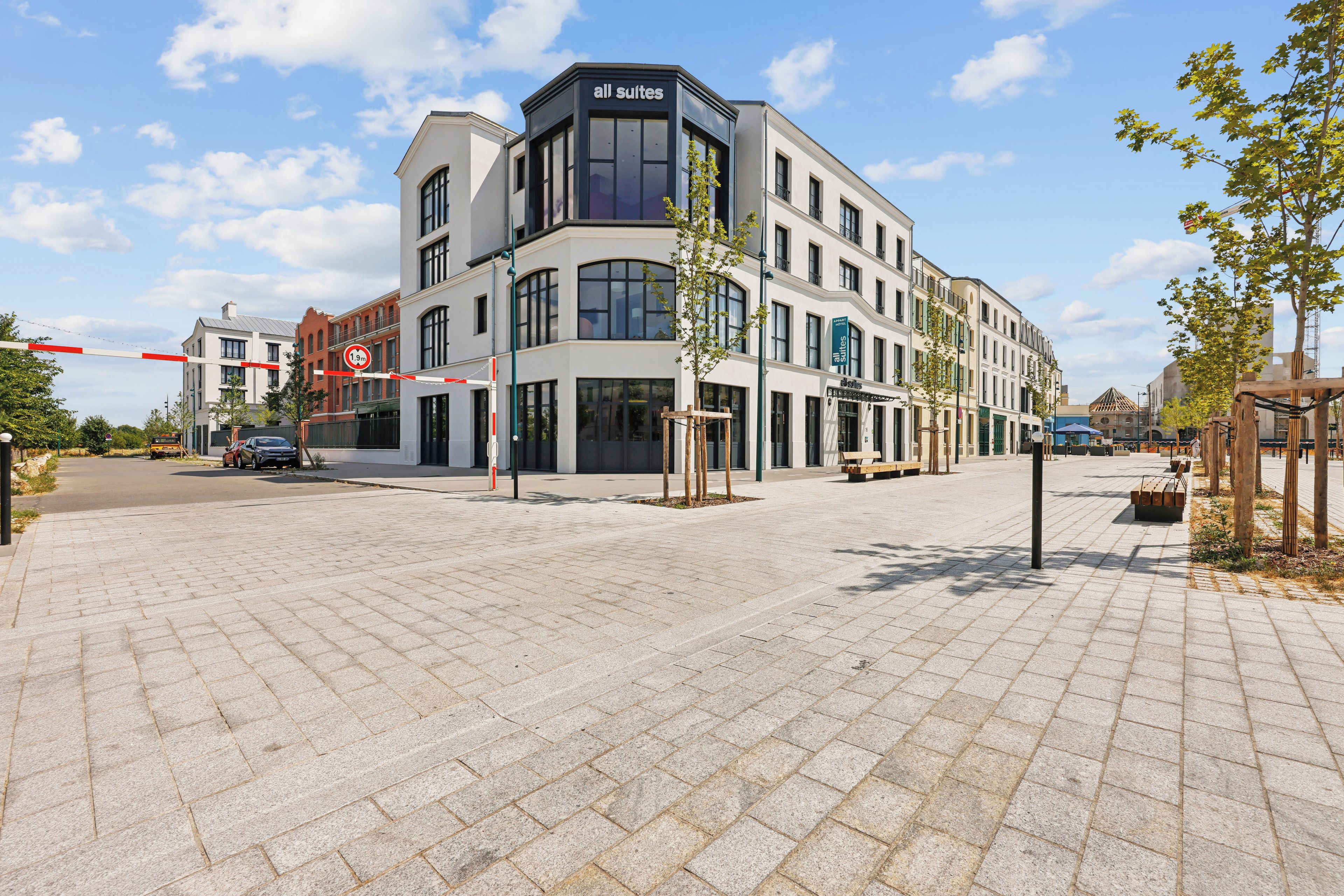A hotel with a modern design, featuring a prominent 'all suites' sign, a gated entrance, and a paved courtyard.