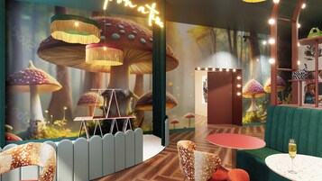 A room with a forest-themed wall mural, a round table with a glass of wine, and a green sofa.