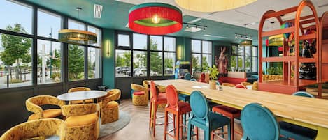 A modern interior with a wooden table, colorful chairs, and large windows offering a view of the street.