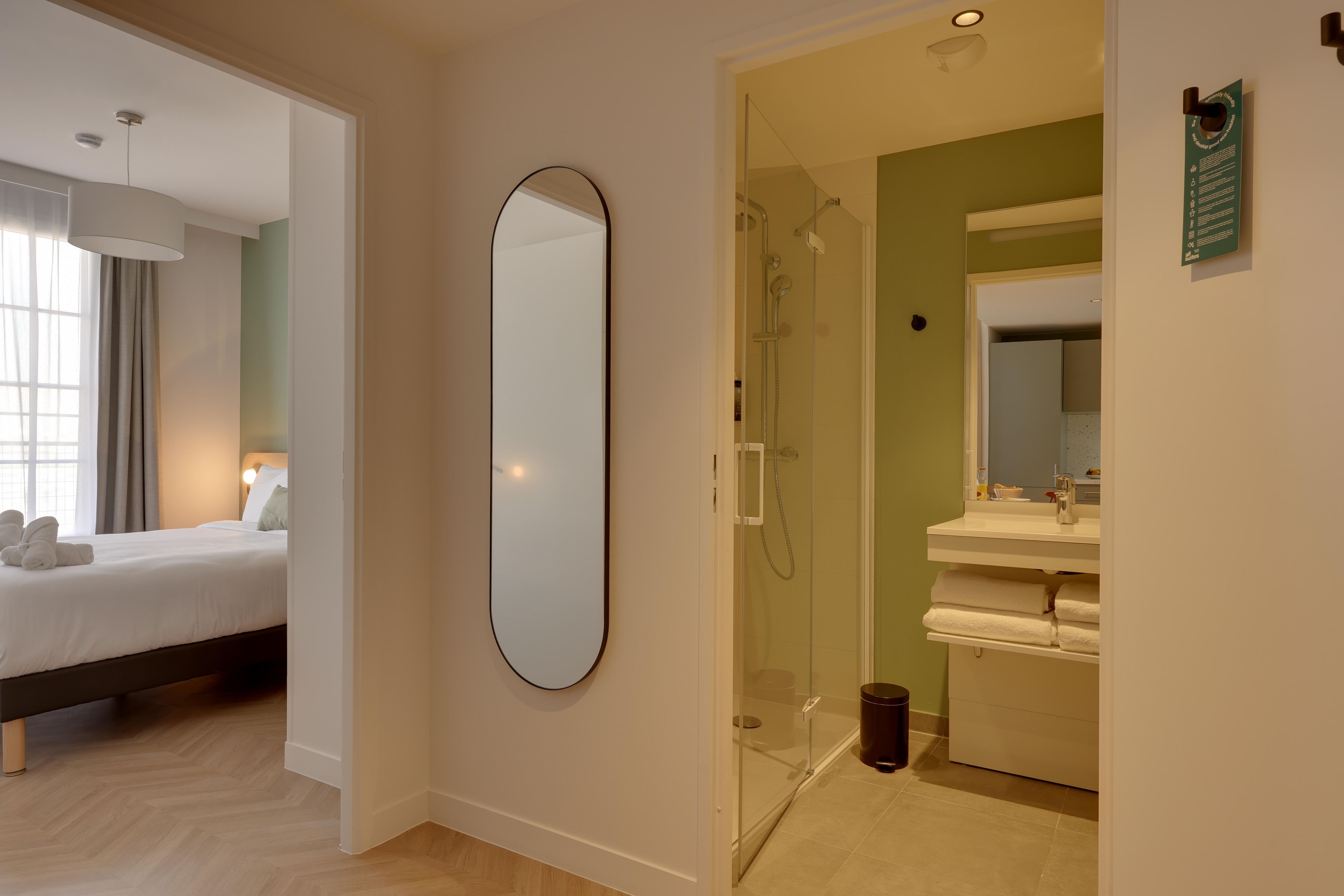 Ein Hotelzimmer mit einem Bett, einem großen Spiegel, einer Dusche und einem Badezimmer inklusive Waschbecken und Spiegel.