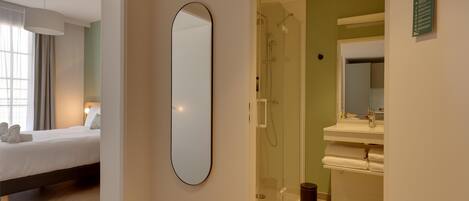 A hotel room with a bed, a large mirror, a shower, and a bathroom with a sink and mirror.