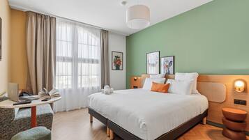 Una habitación de hotel moderna con una cama, un escritorio con una computadora portátil, una silla y una mesita de noche con una lámpara.