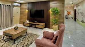 Ein modernes Wohnzimmer mit Fernseher, einer Holz-Unterhaltungsecke, einem rosafarbenen Sofa und einer großen Pflanze.