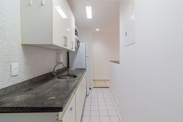 A narrow kitchen with white cabinets, a granite countertop, and a white refrigerator. - 12 Minutes From Copacabana Beach Pl707 (Rio de Janeiro)