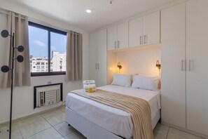 A hotel room with a large bed, white walls, a window with curtains, a radiator, and a wall-mounted light fixture. - 12 Minutes From Copacabana Beach Pl707 (Rio de Janeiro)