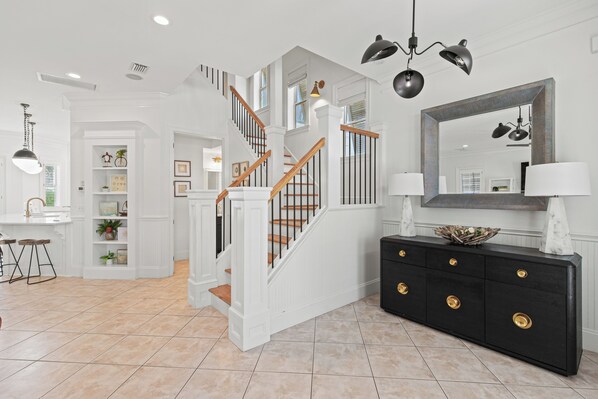 A spacious foyer with a staircase, a black console with gold handles, and a large mirror.