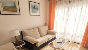 Una sala de estar con un sofá, una mesita de centro y una lámpara. Hay dos cuadros enmarcados en la pared.