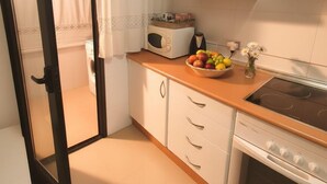 Una cocina compacta con armarios blancos, un microondas, una estufa y un frutero sobre la encimera.