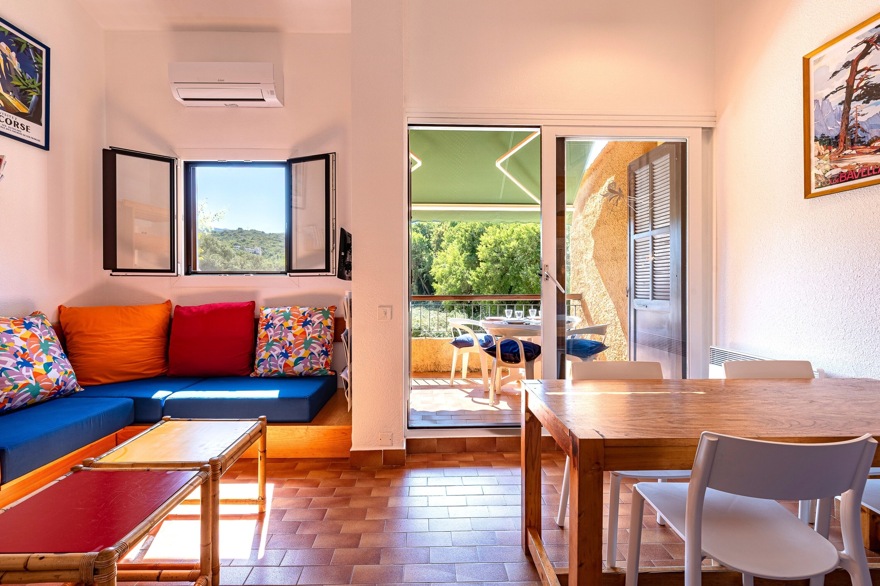 A modern living room with a sofa, a dining table, and a balcony with a view of greenery.