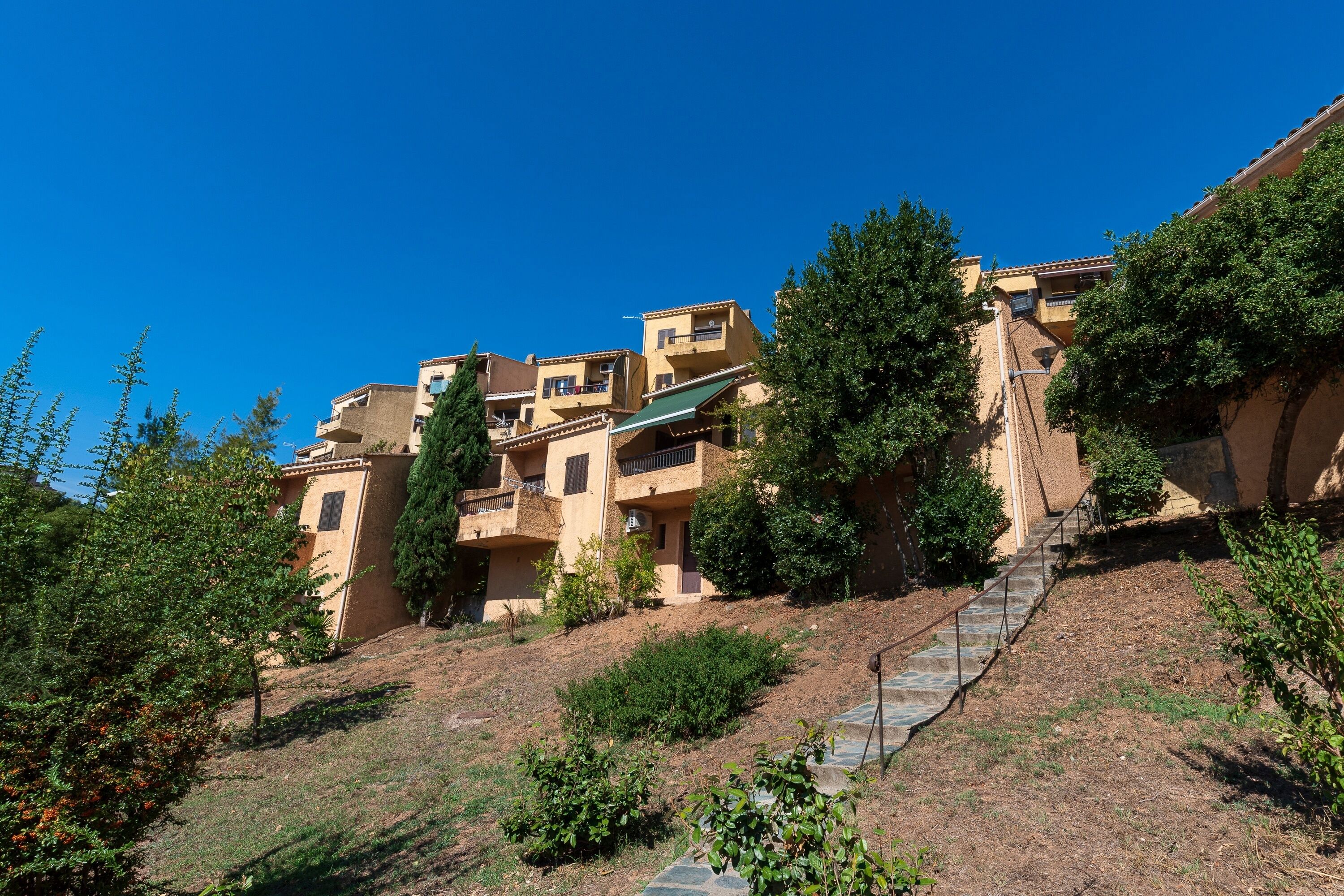 A hillside residential area with terraced houses, a stone staircase, and surrounding greenery.