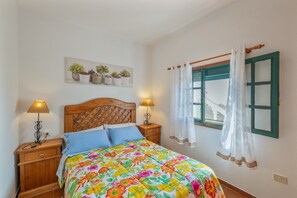 Une chambre à coucher avec un lit en bois, deux tables de chevet avec des lampes, une fenêtre avec des rideaux et une jardinière murale.