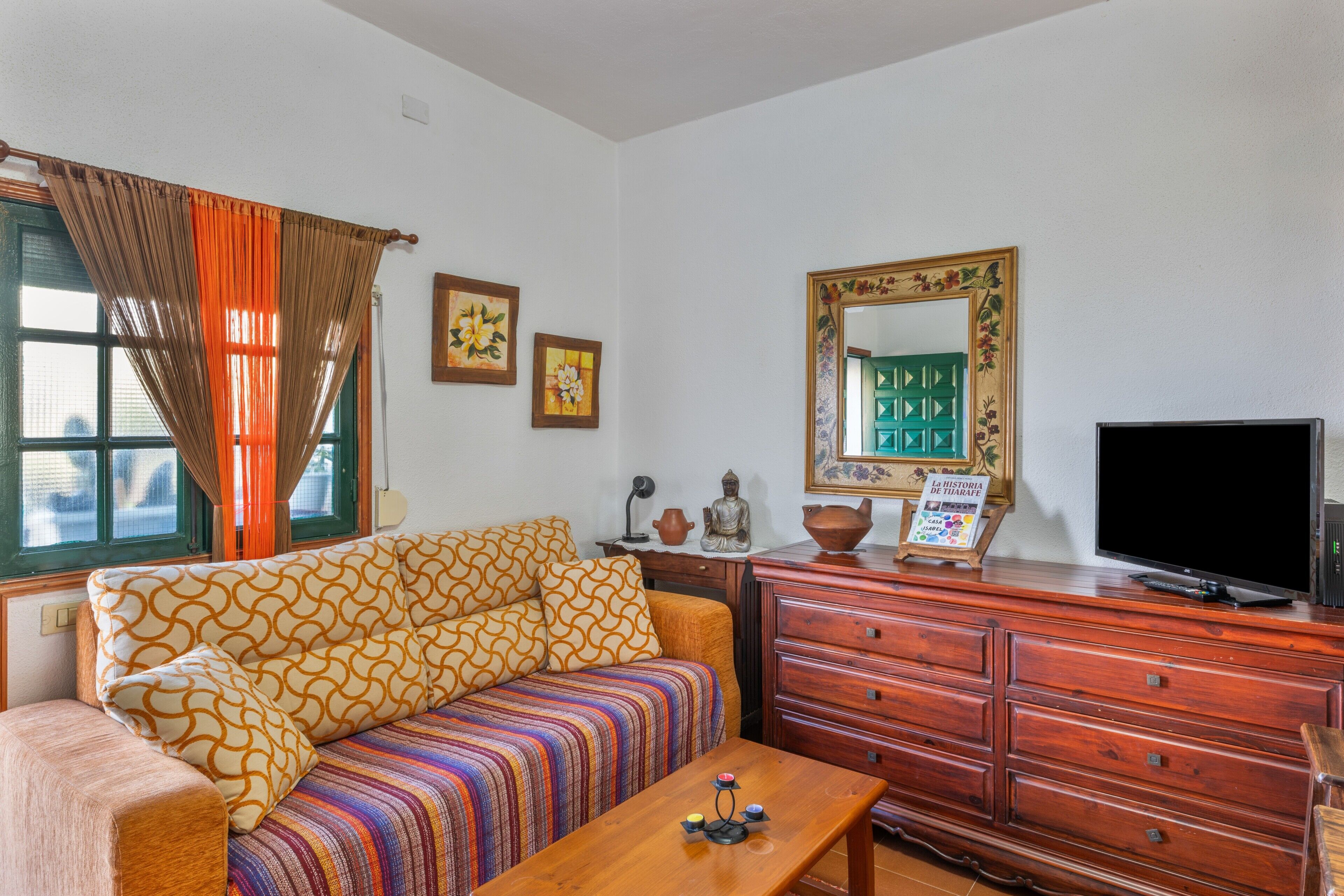 A living room with a sofa, a wooden dresser, a television, and a window with curtains.