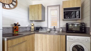 A compact kitchen with wooden cabinets, a built-in microwave, a dishwasher, and a sink. - Lodge 2 - Hibiscus - Jaccuzi Privé (Les Anses-d'Arlet)