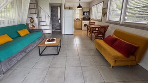En moderne stue med sofa, sofabord, spisebord med stole, et køkkenområde og en trappe.