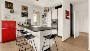 A modern kitchen with a central island, bar stools, a red refrigerator, and a black countertop.