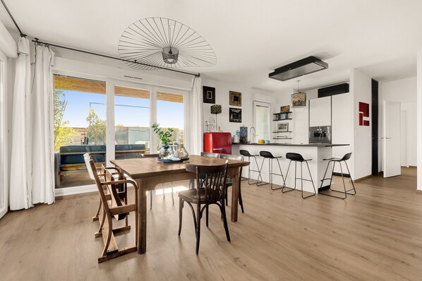 Una cocina moderna con comedor, que incluye una mesa y sillas de madera, una barra con taburetes y un ventanal con cortinas.