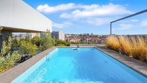 A rooftop swimming pool with a city view, surrounded by greenery and modern architecture.
