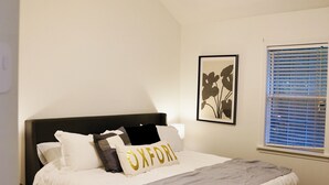 Een slaapkamer met een bed, een plafondventilator, een raam met jaloezieën en een lijst met een afbeelding erop.