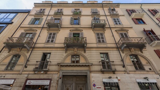 Un bâtiment historique doté de balcons richement décorés, d’une entrée centrale avec une porte ornée et de vitrines au rez-de-chaussée.
