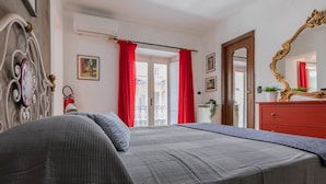 Une chambre à coucher avec un lit, une commode, un miroir et une fenêtre ornée de rideaux rouges.