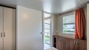 A bedroom with a bed, a window with curtains, a door, and a view of the outdoors.
