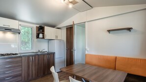 A compact kitchen with a stove, sink, and refrigerator. There is a dining table with chairs and a bench.