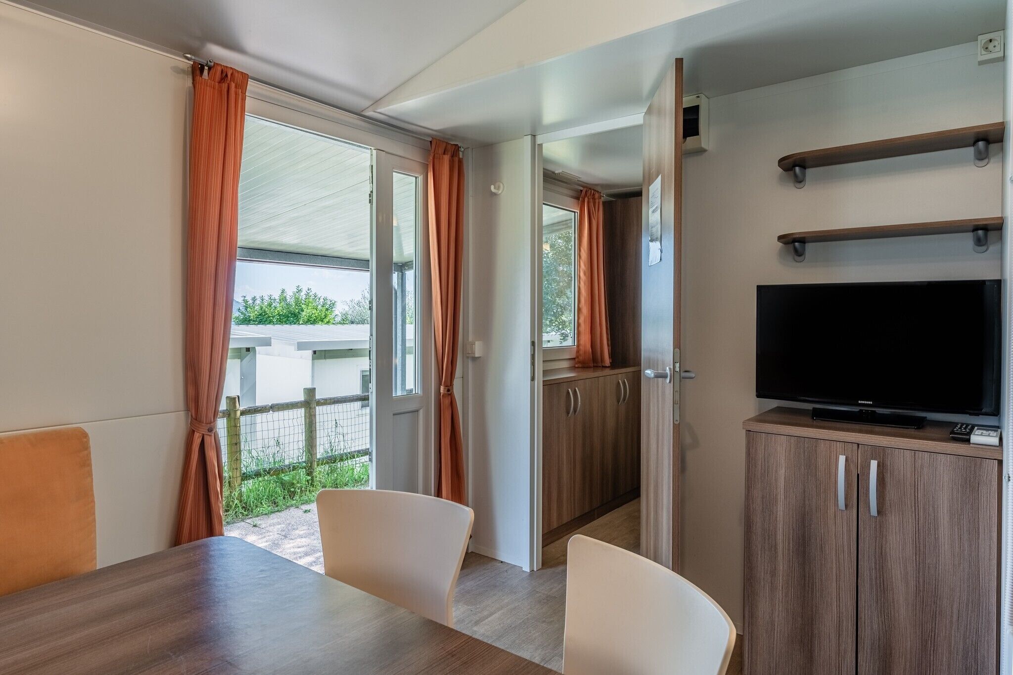 Une pièce comprenant une table à manger, des chaises, un téléviseur posé sur un meuble et une porte coulissante donnant sur l’extérieur.