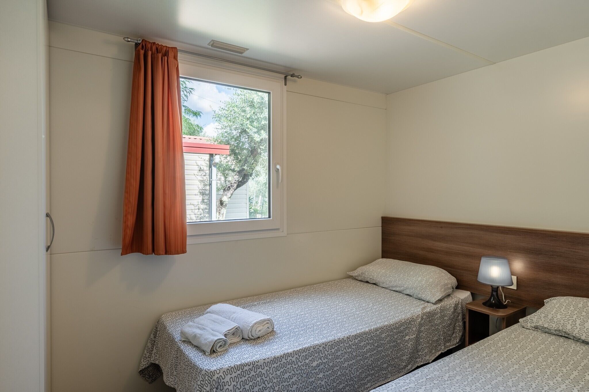 Una cama individual con una colcha estampada, una mesita de noche con lámpara y una ventana con cortina.