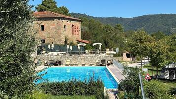 Un edificio de piedra con piscina, rodeado de vegetación y colinas.