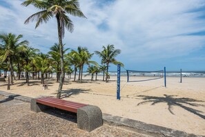 A beach volleyball court with a net, palm trees, and a bench.