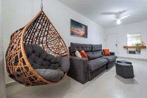 A modern living room with a hanging chair, a sofa, and a ceiling fan.