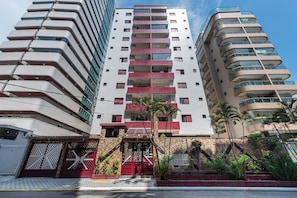 A multi-story hotel with a modern design, featuring balconies, a stone facade, and a gated entrance.